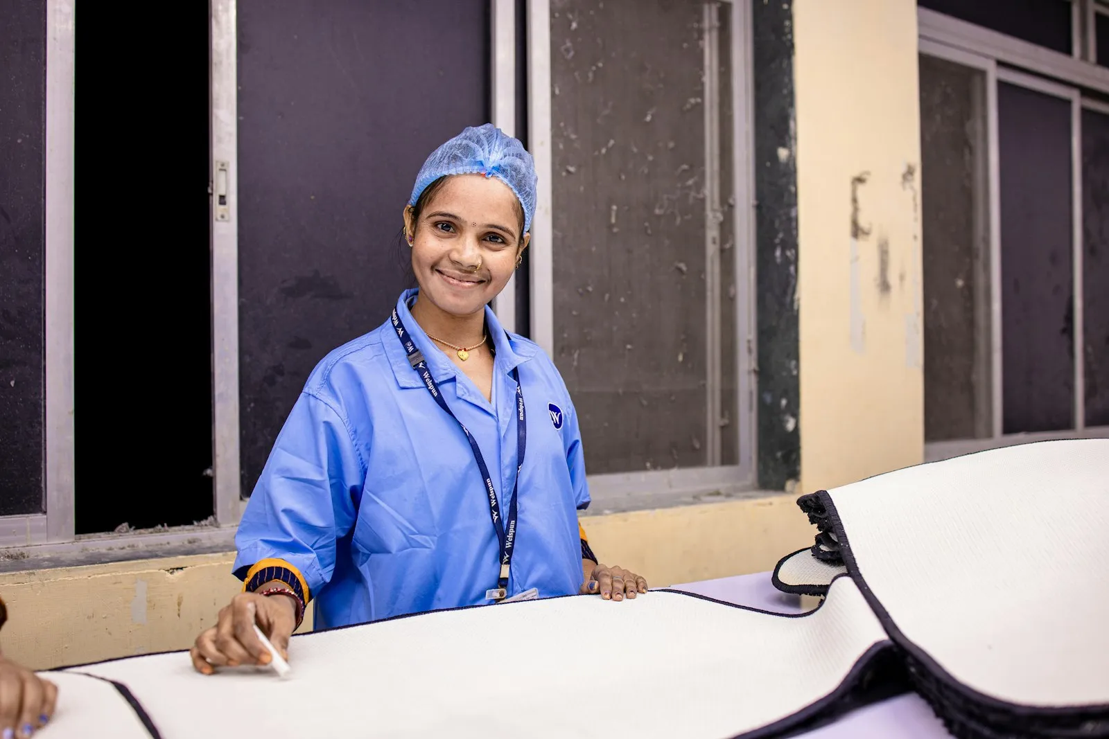 A smiling health worker in blue scrubs and a hair cover