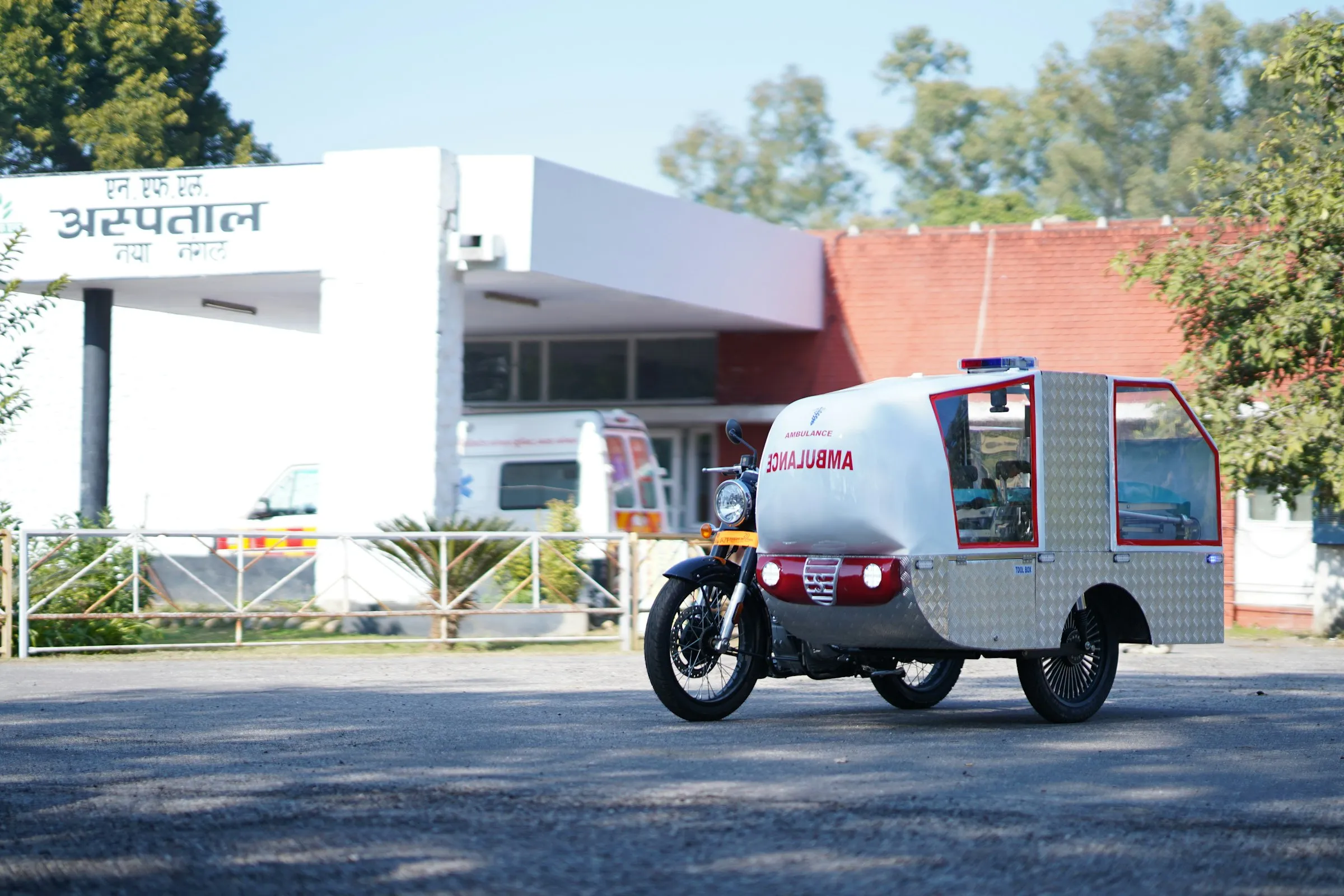 A motorbike ambulance parked outside a hospital in India, with the Hindi sign for hospital above the entrance
