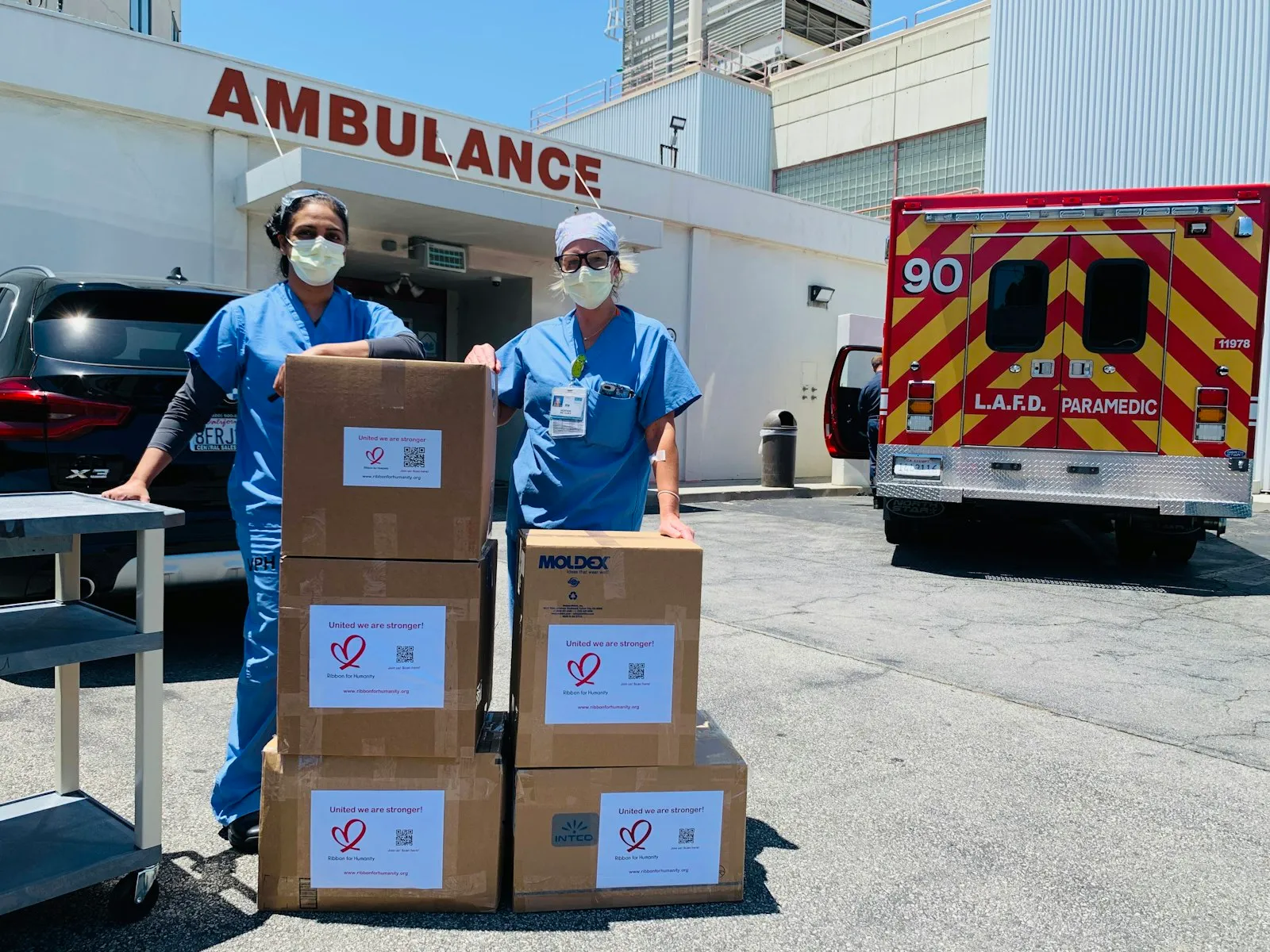 Medical staff standing beside stacked boxes of donated supplies outside a hospital